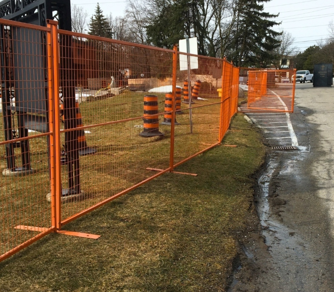 a bright orange temporary fence on a grass boulevard next to a road