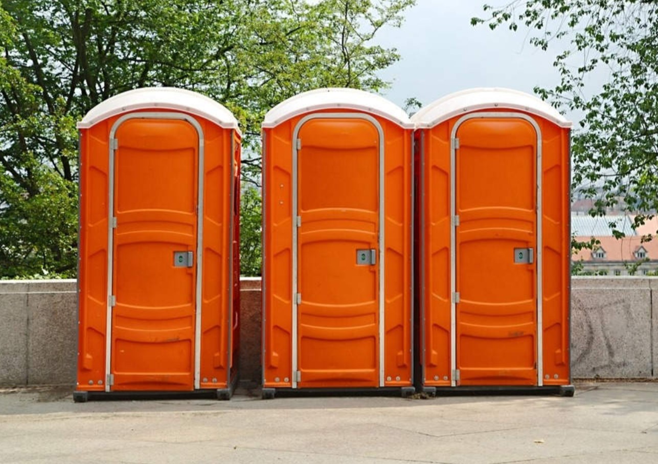 three bright orange portable toilets in a row